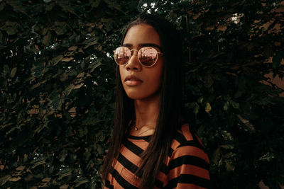 Portrait of beautiful young woman wearing sunglasses against plants