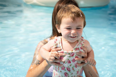 Little girl smiling with the hands of a woman in the middle of a pool