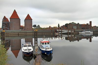 Boats moored at harbor against sky in city