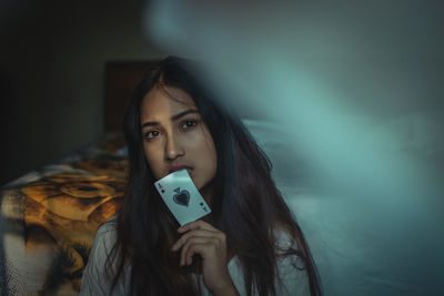 Portrait of young woman holding card while sitting by bed at home