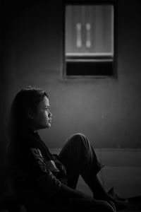 Side view of young woman sitting on chair at home