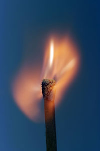 Close-up of burning matchstick over blue background