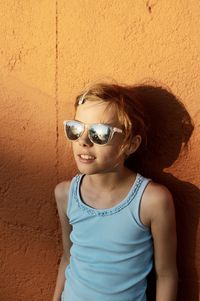 Portrait of young woman wearing sunglasses standing against wall