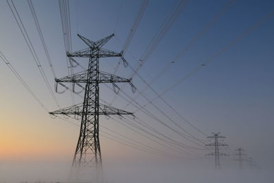 Low angle view of electricity pylon against sky during sunset