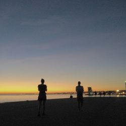 Silhouette people on beach against sky during sunset