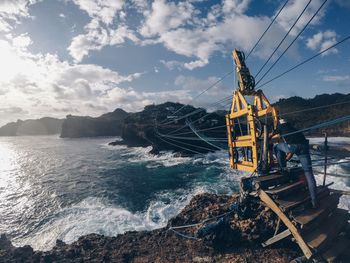 Man standing by overhead cable car over sea against sky