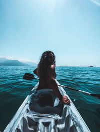 Rear view of woman sitting on sea against sky