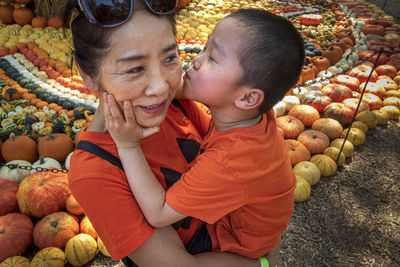 High angle view of grandson kissing grandmother standing against pumpkins