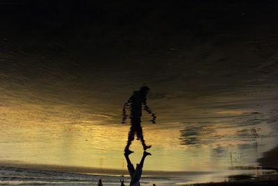 Upside down image of man walking on shore during sunset