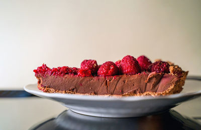 A piece of a delicious chocolate tart with raspberry on the white plate against white background