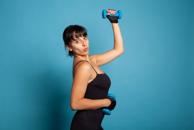 Young woman lifting dumbbell against blue background