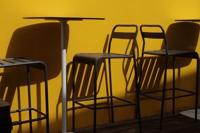 Empty chairs and table against yellow wall at outdoors cafe