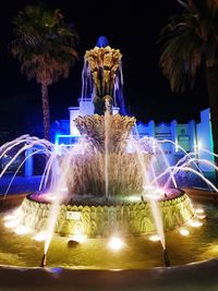 Illuminated fountain against light at night