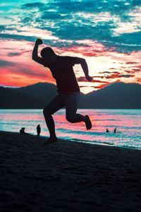 Silhouette men jumping on beach against sky during sunset
