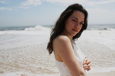 Portrait of beautiful woman standing at beach against sky