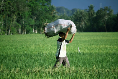 Farmer carrying sack on field against tree