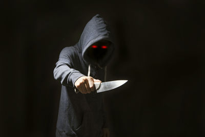 Thief holding knife against black background