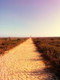 Dirt road on field against clear sky