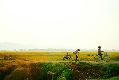 People walking on grassy field against sky