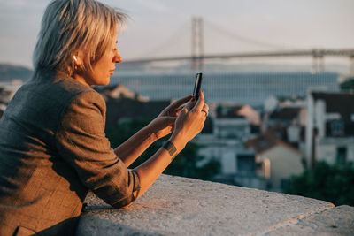 Side view of man using mobile phone against sky