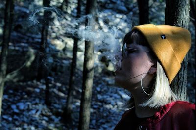 Woman exhaling smoke against tree