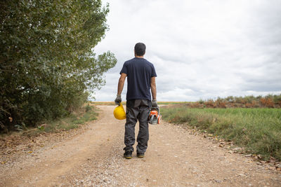 Rear view of man walking on road amidst field