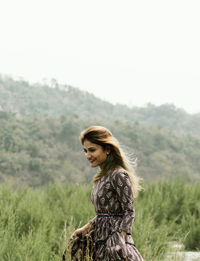 Smiling woman standing on field against sky