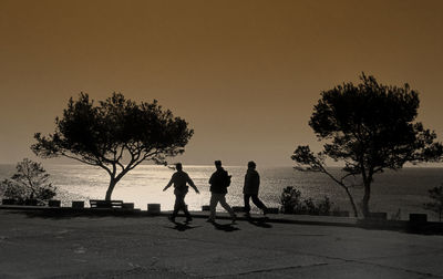Silhouette people walking on road against sea