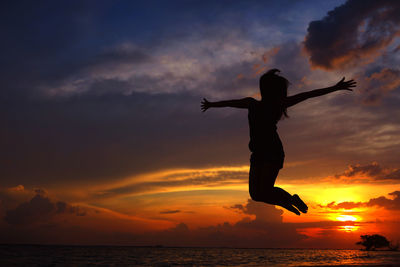 Low angle view of silhouette woman jumping against orange sky