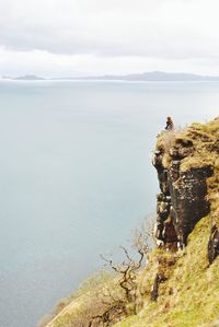 Woman sitting on cliff against sea