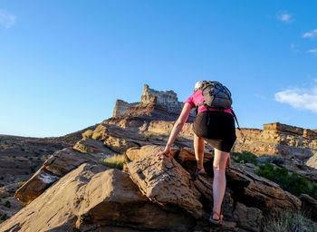 Rear view of woman standing on rock against blue sky