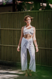 Portrait of young woman standing against fence