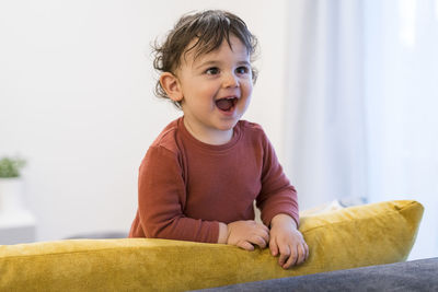 Cheerful boy looking away while standing on sofa at home
