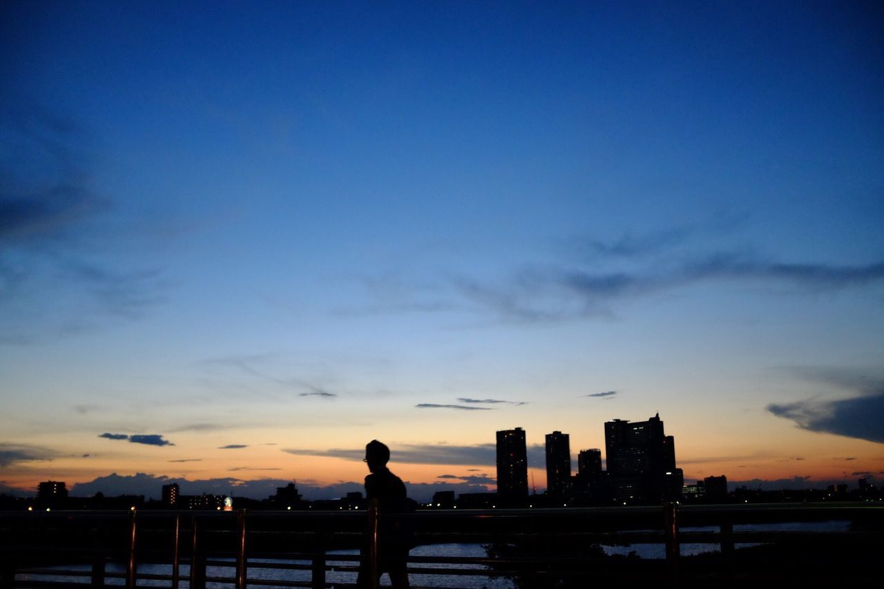 silhouette, sunset, sky, built structure, architecture, building exterior, lifestyles, standing, leisure activity, men, dusk, city, person, railing, cloud - sky, blue, orange color