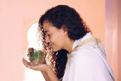 Woman smelling while holding drink against wall