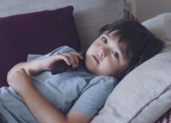 Portrait of boy holding remote control while watching tv on sofa at home