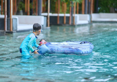 Boy and girl play floater in big swimming pool near under water stairs on blur sofa background 