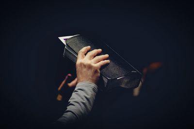 Close-up of hand on book against black background
