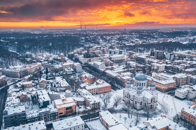 Aerial view of snow covered townscape against cloudy sky during sunset