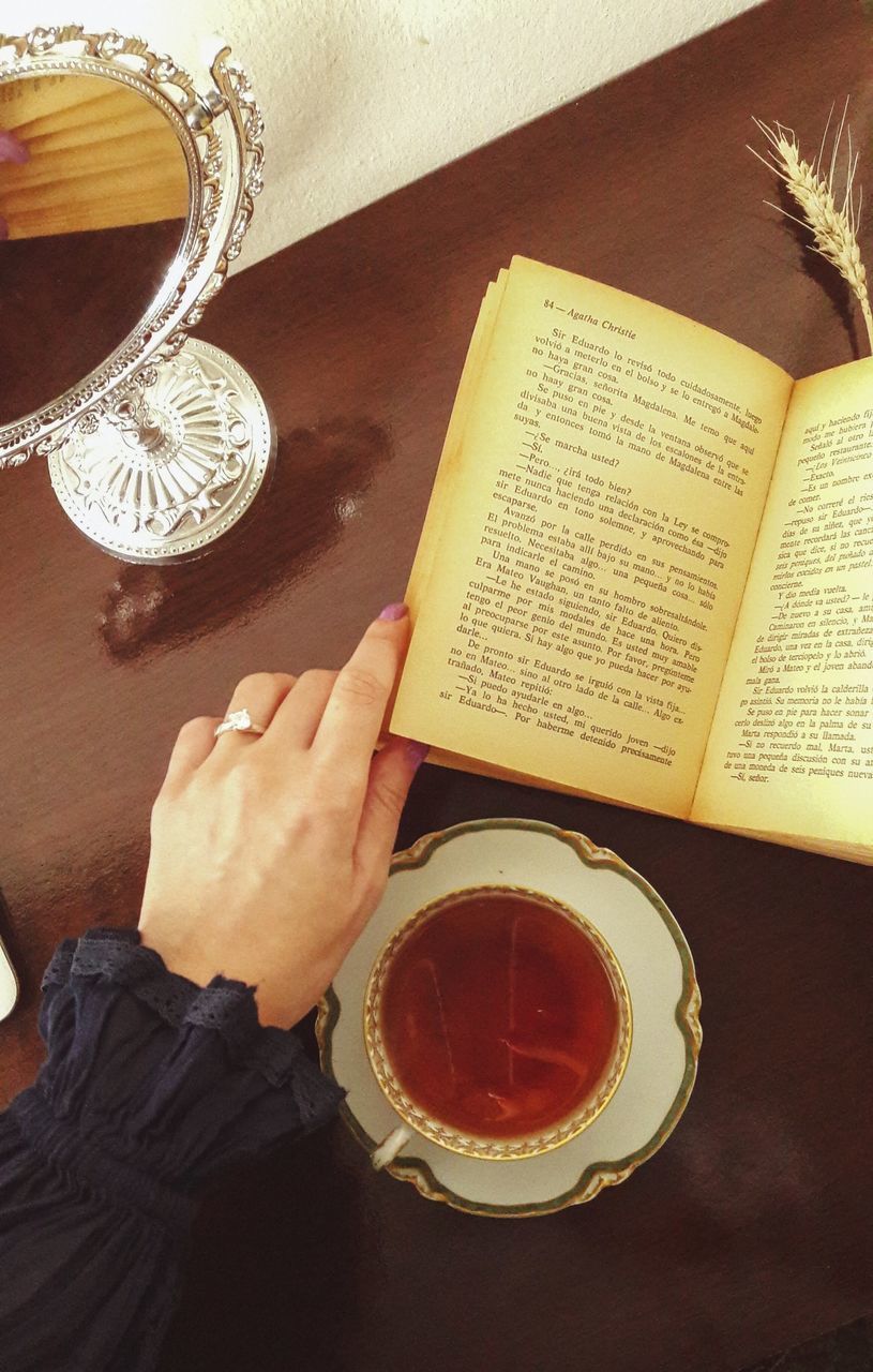 HIGH ANGLE VIEW OF HAND HOLDING BOOK ON TABLE IN KITCHEN