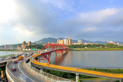 Bridge over river amidst buildings in city against sky