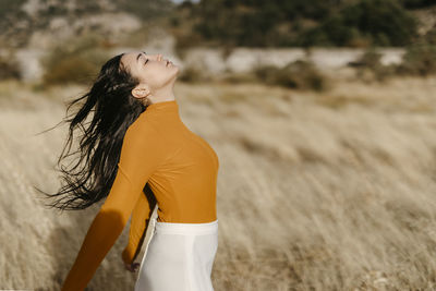 Carefree young woman with eyes closed standing in field during windy day