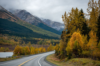 Road amidst trees and mountains against sky during autumn