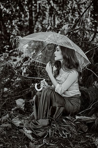 Woman holding umbrella on field in forest