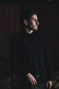 Young man standing against wall at night