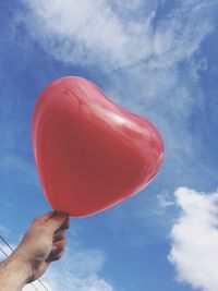 Cropped hand holding heart shape balloon against sky