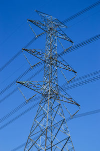 Low angle view of electricity pylon against blue sky