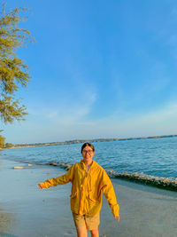 Portrait of young man standing at beach against sky