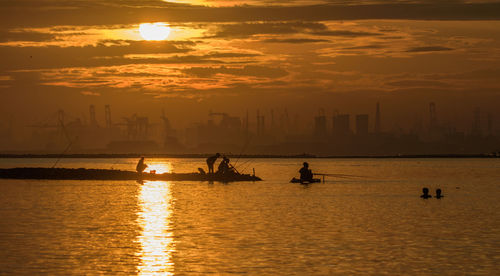 Silhouette people fishing in river against sky during sunset