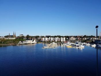 Sailboats moored in harbor against clear blue sky